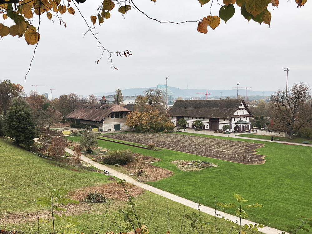 In the foreground: a dry meadow; in the middle: lawn and iris flower collection; in the background: historical farm buildings by the architect Melchior Berri (1801-1854), the left one today used as a restaurant.